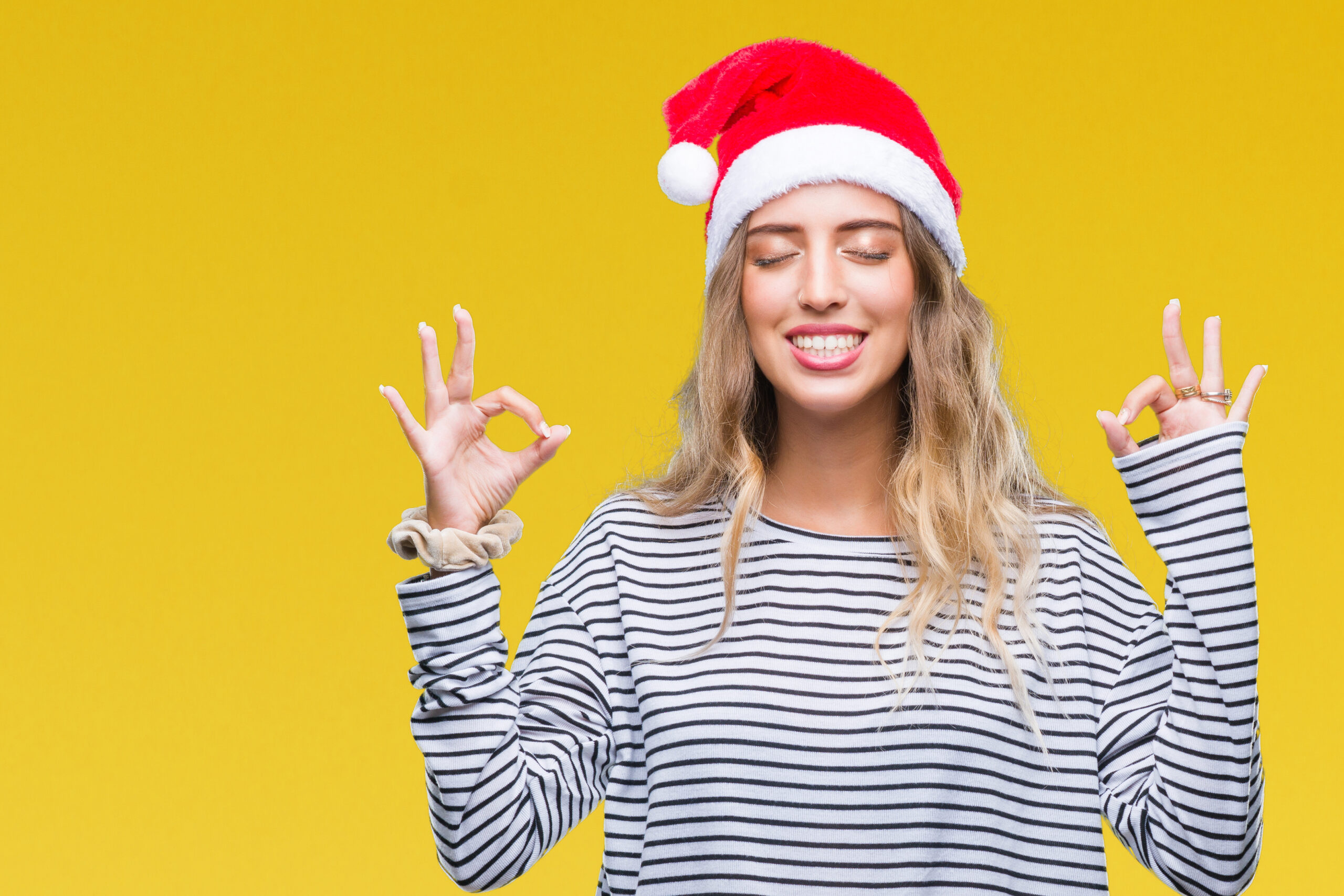 Beautiful young blonde woman wearing christmas hat over isolated background relax and smiling with eyes closed doing meditation gesture with fingers. Yoga concept.