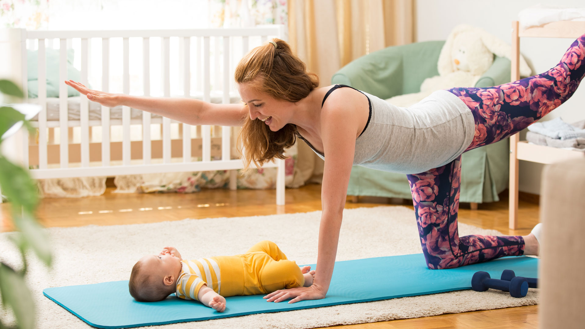 Woman works out postpartum with baby on yoga mat